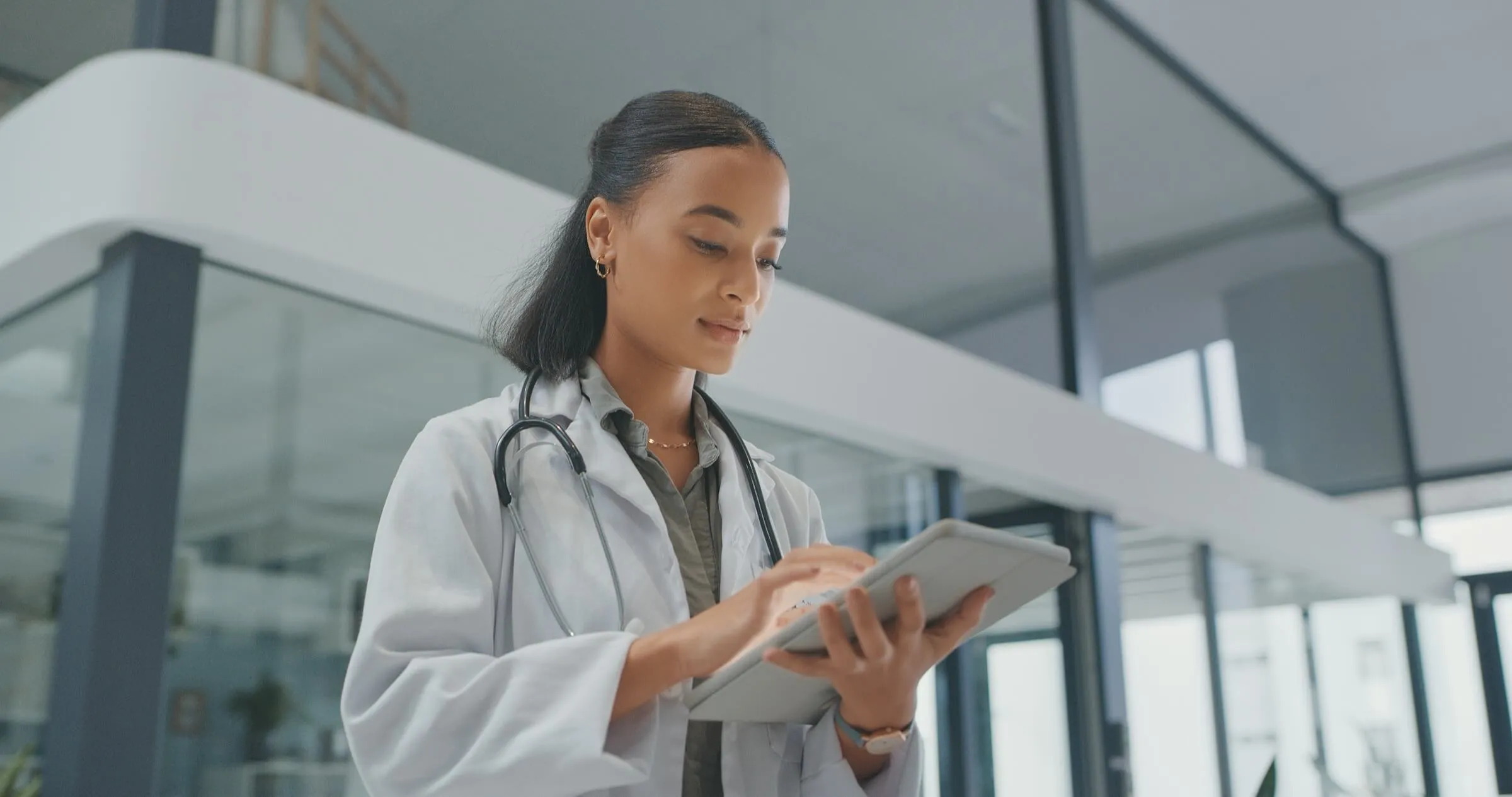 Medical professional in white coat reviewing data on digital device in modern clinic setting.